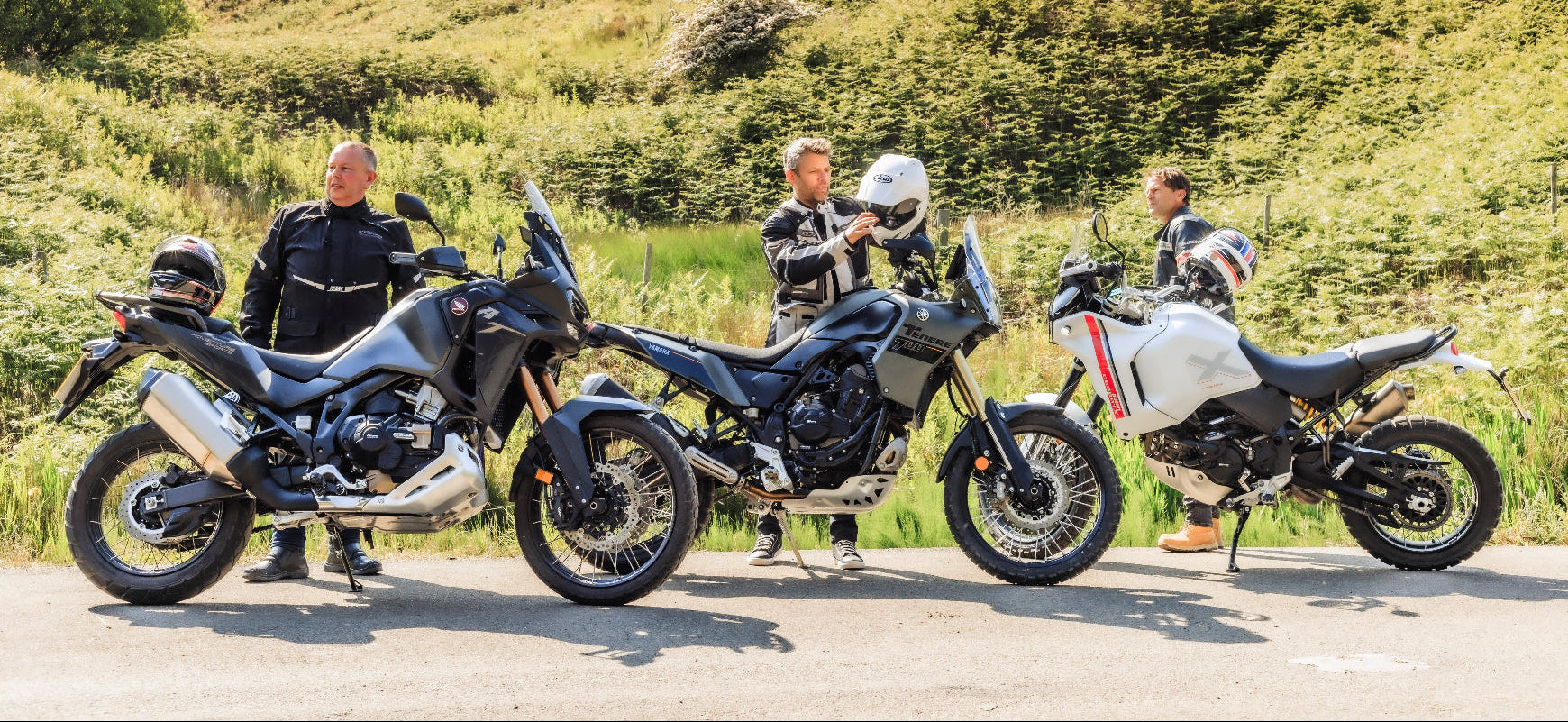 Three motorcycles parked on a road with a scenic background
